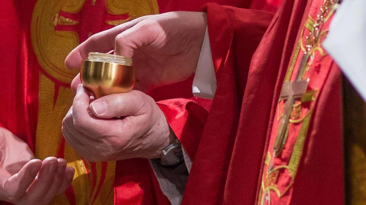 Weihbischof Schwaderlapp taucht seinen Daumen in ein Gefäß mit Chrisamöl