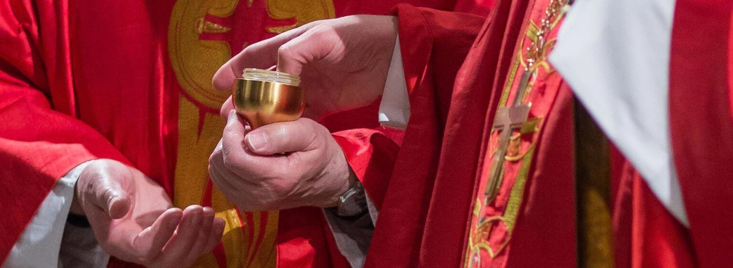 Weihbischof Schwaderlapp taucht seinen Daumen in ein Gefäß mit Chrisamöl