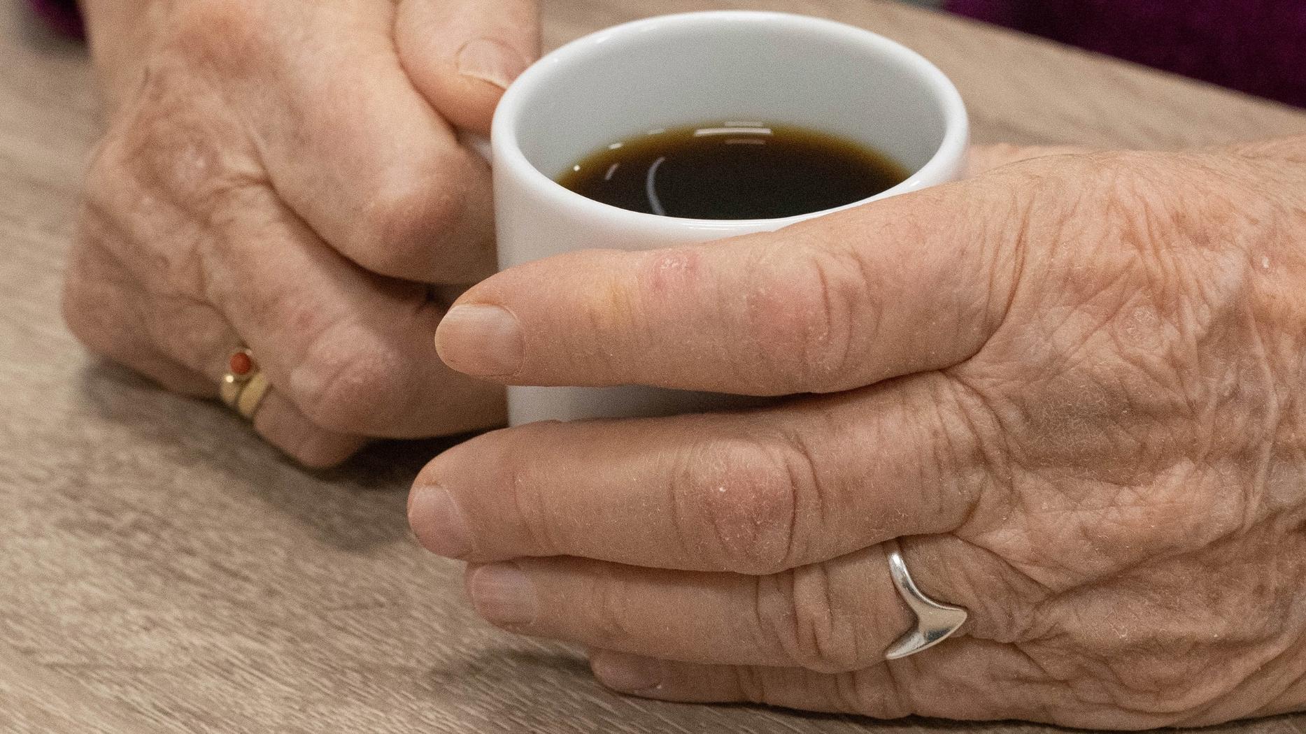 alte Hände halten eine Kaffeetasse in der Hand