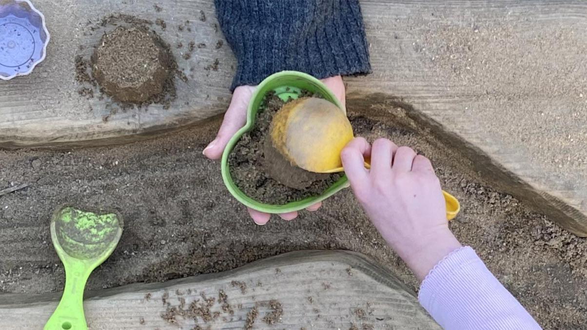 Hände: Erzieherin und Kind spielen mit Sandförmchen.