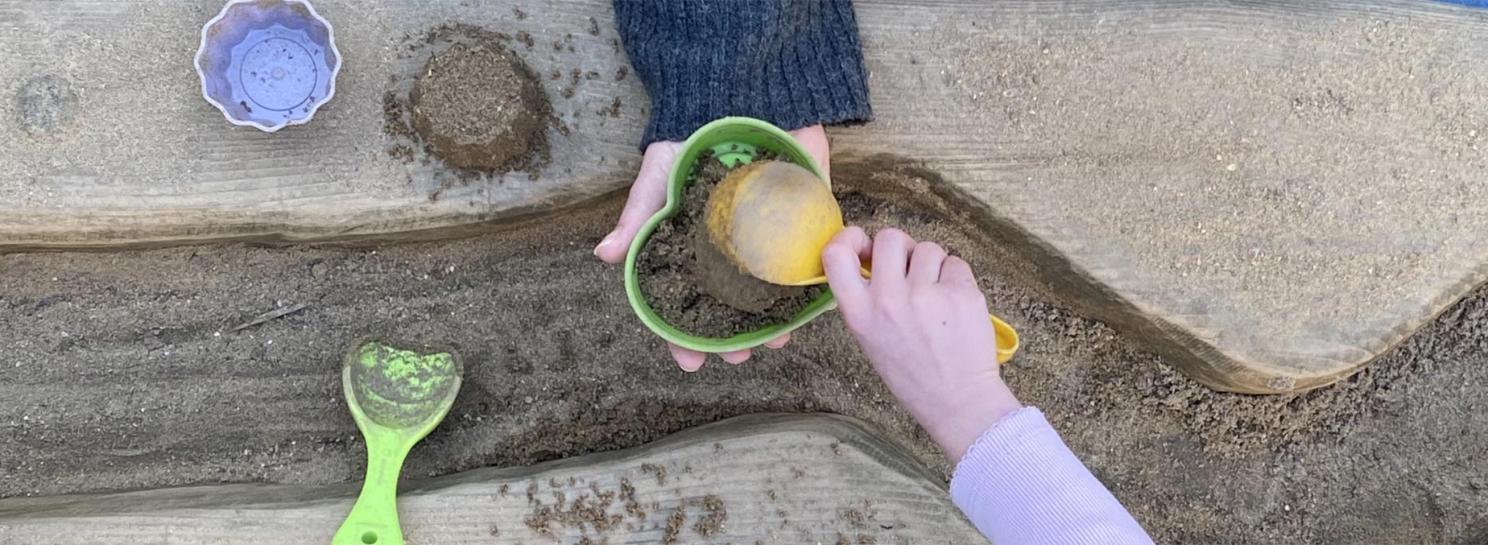 Hände: Erzieherin und Kind spielen mit Sandförmchen.